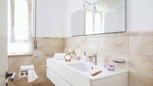 A bathroom with a large mirror, a sink, a towel rack, and a window. - Comfortable apartment  (Pozzallo)