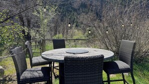 Mesa redonda exterior de mimbre con sillas, rodeada por una cerca y con vistas a un paisaje montañoso.