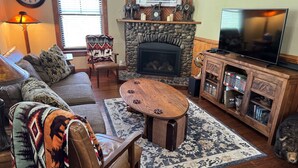 Una sala de estar acogedora con chimenea de piedra, televisor, sofá, alfombra estampada y una silla decorativa.