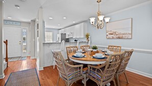 A dining area with a round table, wicker chairs, and a chandelier. - Andreas Place Spacious Family Getaway, Easy Beach Access, Pool (Kure Beach)