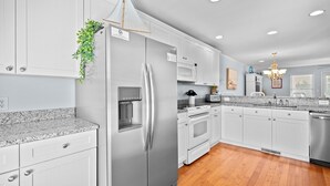 A modern kitchen with white cabinets, stainless steel appliances, granite countertops, and a wooden floor. - Andreas Place Spacious Family Getaway, Easy Beach Access, Pool (Kure Beach)