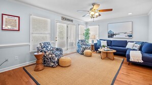 A living room with a blue sofa, two blue patterned chairs, a wooden coffee table, and a ceiling fan. - Andreas Place Spacious Family Getaway, Easy Beach Access, Pool (Kure Beach)