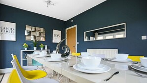 A dining area with a long table set for six, white chairs, and a modern decor. - 🌟Large house with Free Parking, Smart TV & Garden🌟 (Bletchley)
