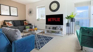 A modern living room with a flat-screen TV, a clock, and a sofa. - 🌟Large house with Free Parking, Smart TV & Garden🌟 (Bletchley)