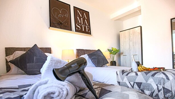 A hotel room with two beds, a hairdryer, towels, a fruit bowl, and a mirror. - 🌟Large house with Free Parking, Smart TV & Garden🌟 (Bletchley)