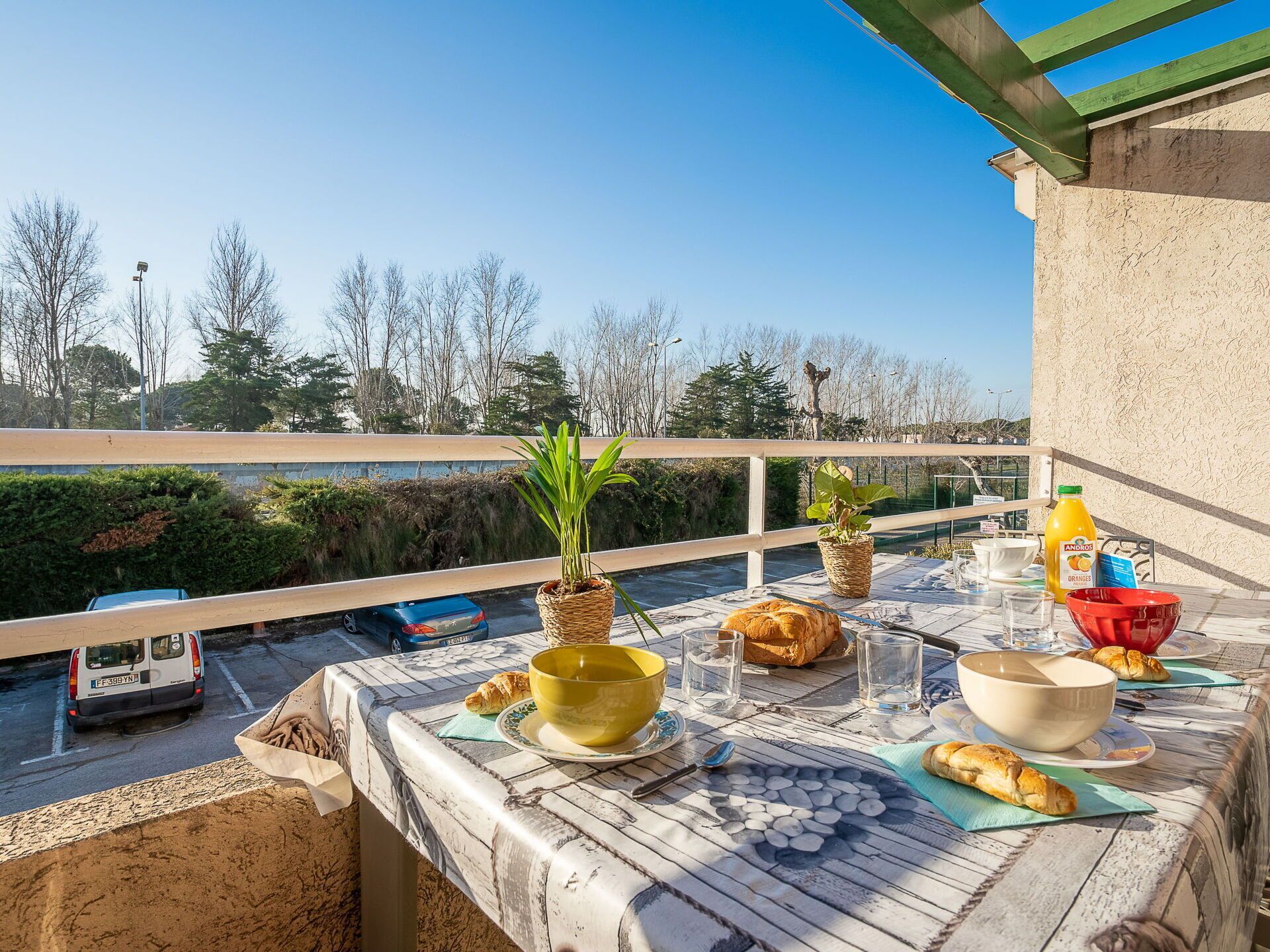 A balcony with a table set for breakfast, including croissants, bread, and a bottle of orange juice.