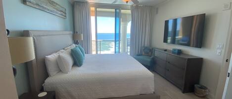 Un dormitorio con cama, ventilador de techo, televisión, cómoda y vista al océano.