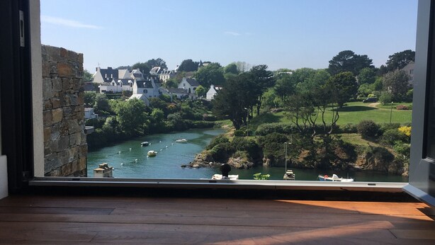 Ein Zimmer mit großem Fenster, das auf einen Fluss, Grünflächen und Gebäude blickt.