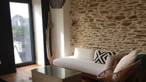 Ein modernes Wohnzimmer mit einer Steinwand, einem Glastisch, einem weißen Sofa mit gemusterten Kissen, einem Korbstuhl und einem Kuhfellteppich.
