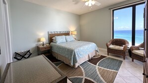 Ein Schlafzimmer mit Bett, Deckenventilator, Nachttisch, Stuhl und Meerblick.