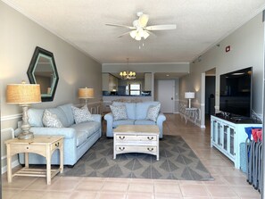 Ein Wohnzimmer mit Sofa, Couchtisch und TV-Standfuß, im Hintergrund eine Küche und ein Deckenventilator.