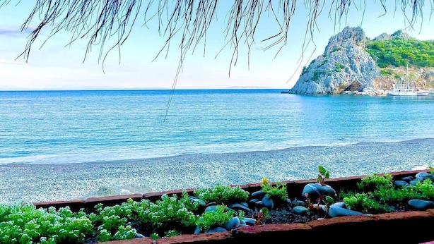 Vista costera con un promontorio rocoso, mar tranquilo y una playa de piedras.