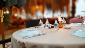 Mesa lista para comer con cristalería transparente, una vela y una botella de agua.