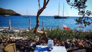 Una mesa frente al mar con mantel a cuadros, un florero y una silla de mimbre.