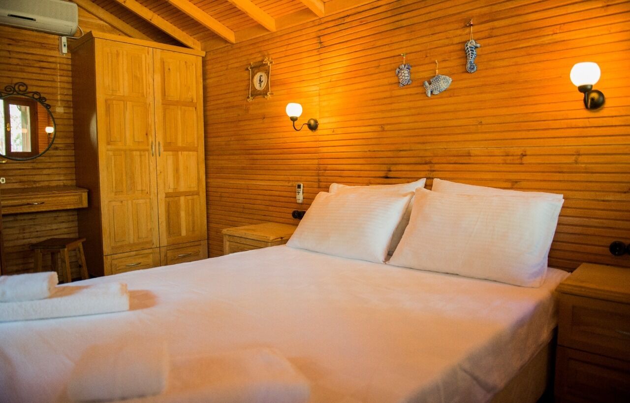 A wooden-paneled room with a bed, a nightstand, a wardrobe, and wall-mounted light fixtures.