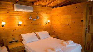 Habitación de cabaña de madera con una cama, mesitas de noche, luces fijadas a la pared y un equipo de aire acondicionado.