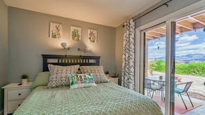 A bedroom with a bed, bedside tables, a nightstand, a window with a view of the outdoors, and wall art.