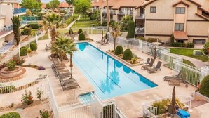 A swimming pool surrounded by lounge chairs and palm trees, with apartment buildings in the background.