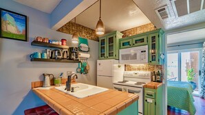 A kitchen with a central island, green cabinets, a microwave, and a stove. There are hanging utensils and a coffee maker on the island.