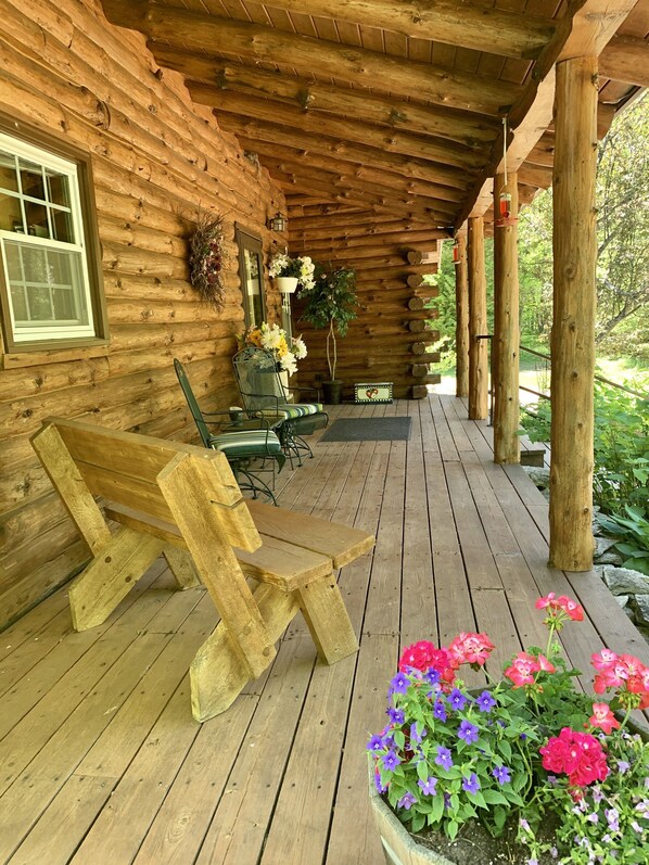 A wooden cabin with a porch, a bench, and a potted plant with flowers. - Rustic Log Home located near Baileys Harbor (Baileys Harbor)