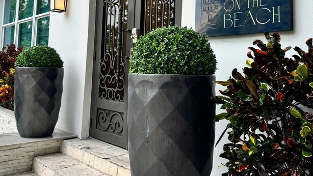 A building entrance with a large arched door, two potted plants, a sign reading "RENZI ON THE BEACH", and a wall-mounted light fixture. - Renzzi On The Beach (Miami Beach)