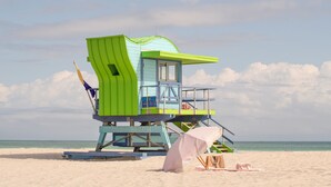 A lifeguard tower with a blue and green color scheme, located on a sandy beach with the ocean in the background. - Renzzi On The Beach (Miami Beach)