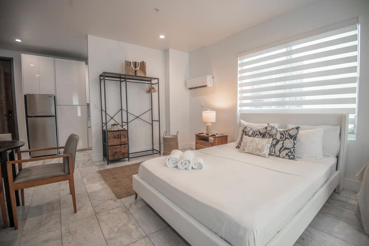 Una habitación de hotel con una cama grande, un escritorio, una silla, un armario y una ventana con persianas.
