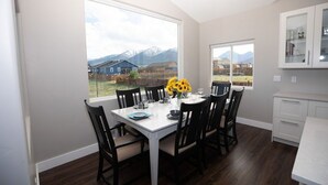 A dining area with a table set for six, large windows offering a view of houses and mountains, and a white cabinet above the table.