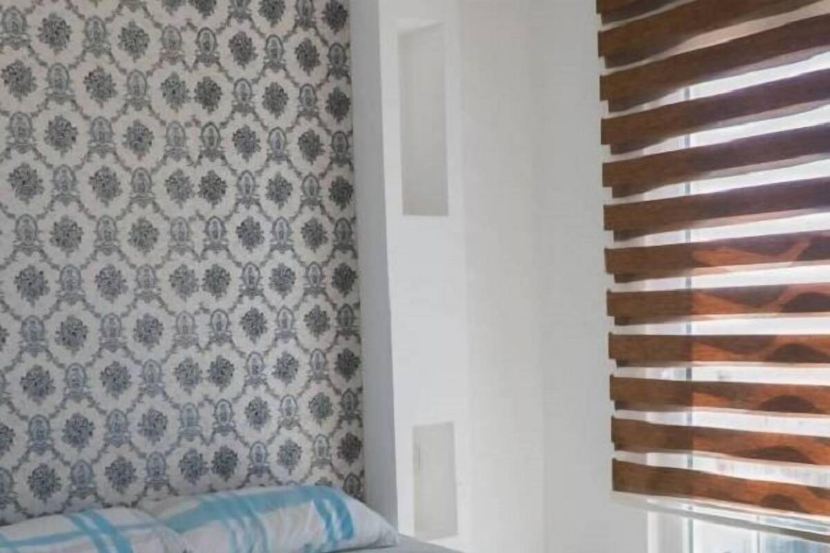A bed with a patterned headboard, a window with wooden blinds, and a view of the city.