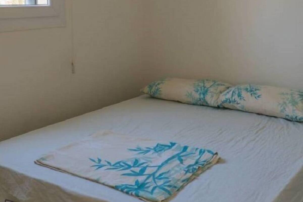 A single bed with a white mattress and a blue leaf-patterned pillow.