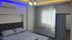 A modern bedroom with a tufted headboard, a bed with grey bedding, a bedside table, and a wardrobe.