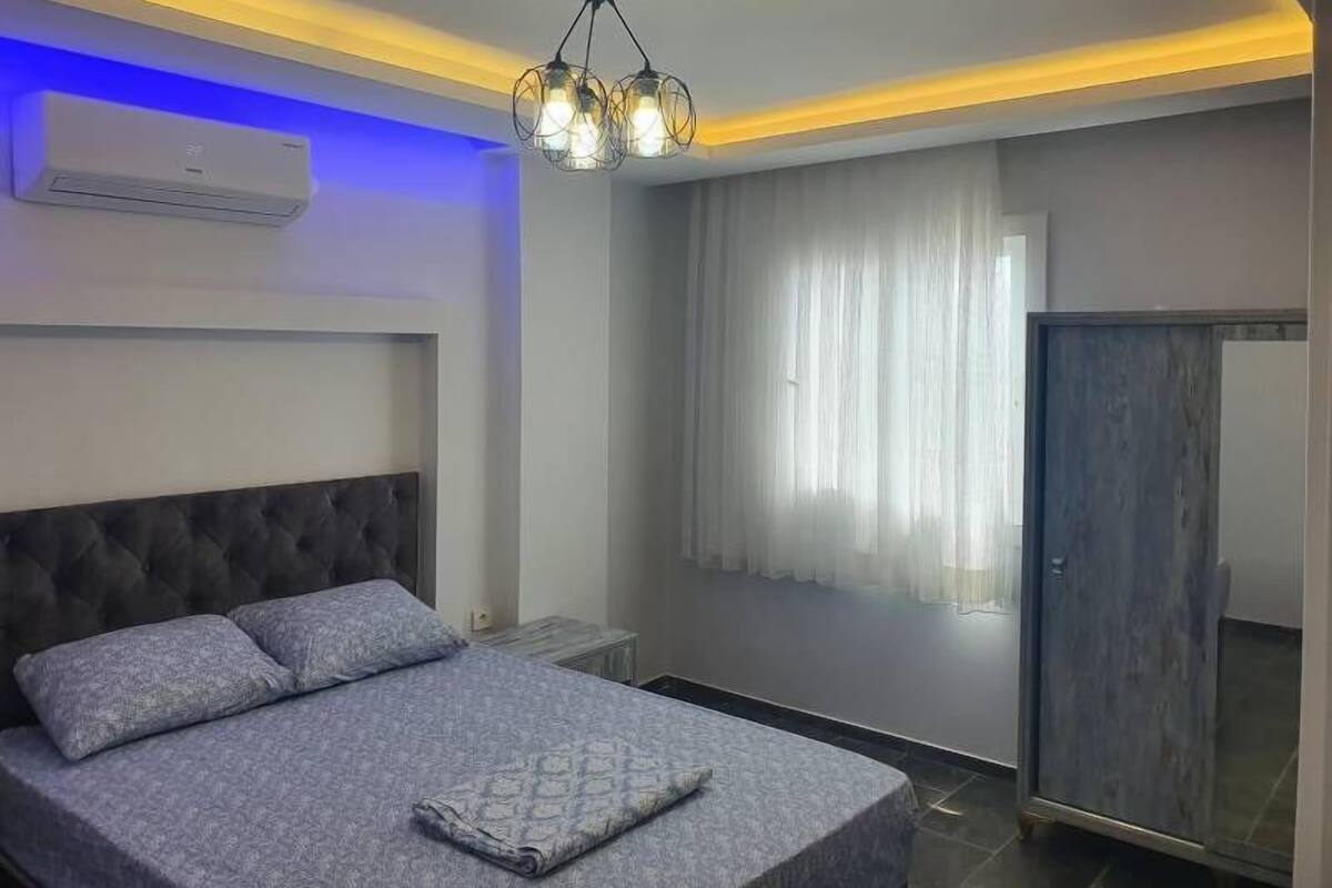 A modern bedroom with a tufted headboard, a bed with grey bedding, a bedside table, and a wardrobe.