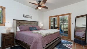 Un dormitorio con una cama de madera, ventilador de techo, ventana con vistas y puerta que da al exterior.