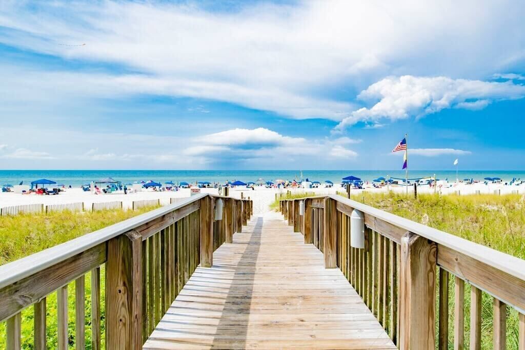 A wooden boardwalk leading to a beach with a flag in the distance.