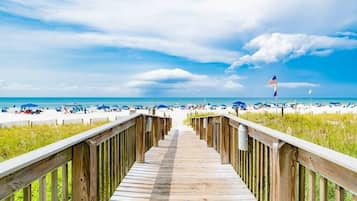 A wooden boardwalk leading to a beach with a flag in the distance.