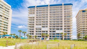 A high-rise hotel with multiple balconies, located near a beach with palm trees and a sandy area. - High Speed Wi-fi, Corner Unit w/Beach and Pool Views (Orange Beach)