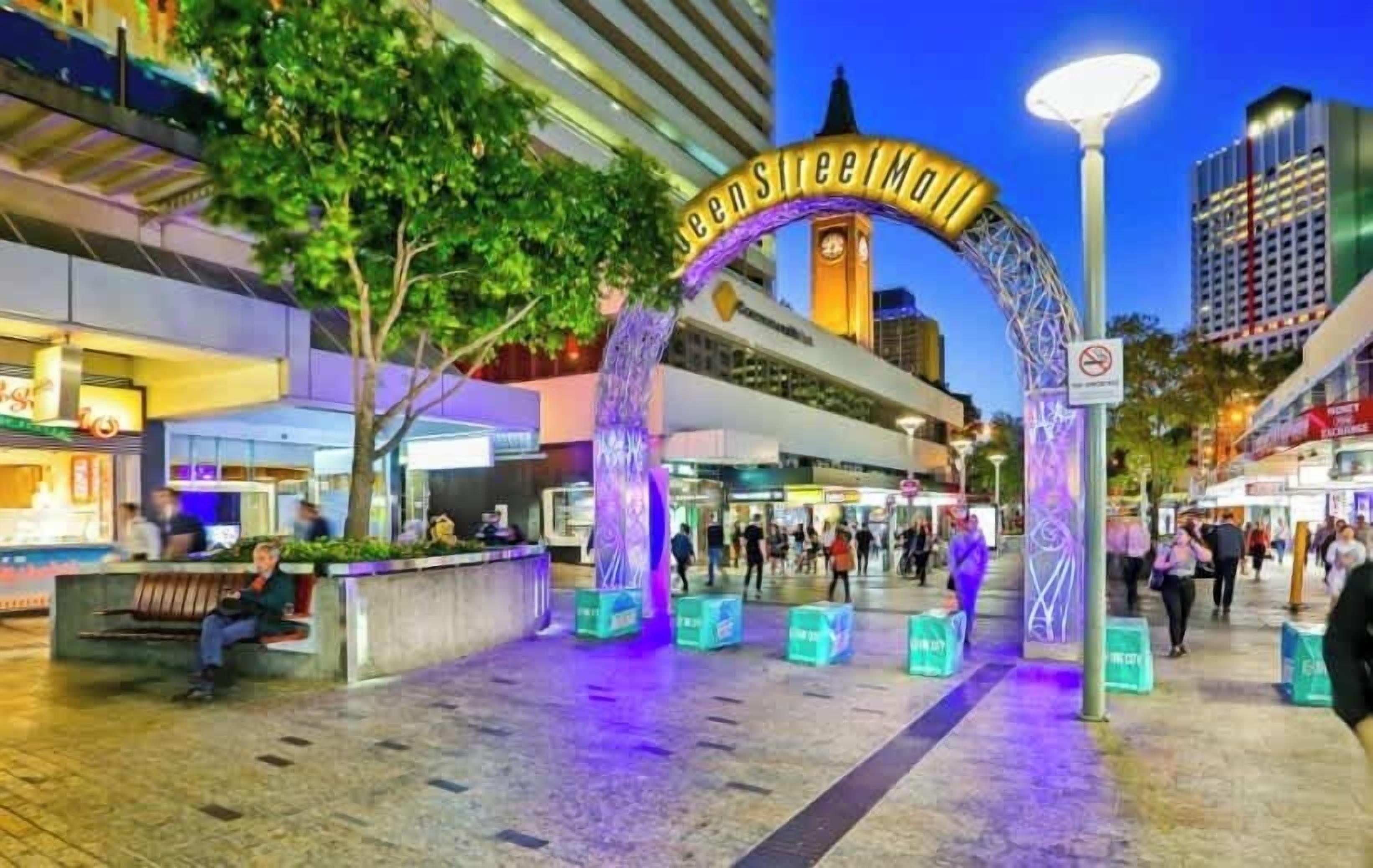 A pedestrian entrance with a sign reading 'Queen Street Mall,' surrounded by shops and a clock tower.