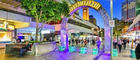 A pedestrian entrance with a sign reading 'Queen Street Mall,' surrounded by shops and a clock tower.