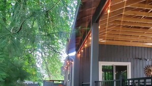 A covered outdoor patio with a wooden deck, a brick pathway, and a blue plastic chair.