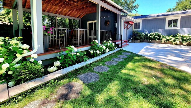 A house with a covered porch, a front yard with stepping stones, and a garden with white flowers.