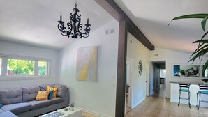 A spacious living room with a grey sofa, a coffee table, and a chandelier. There is a hallway leading to other rooms.