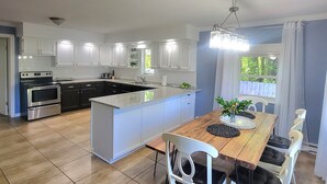 A modern kitchen with white cabinets, a central island, and a dining area with a wooden table and white chairs.