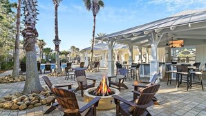 An outdoor seating area with a fire pit, surrounded by chairs and tables, under a covered patio with a pool in the background. - Your Luxury 30A Escape with Private Pool & Coastal Charm (Santa Rosa Beach)