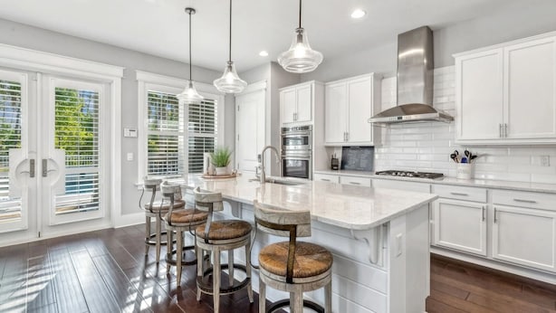 A modern kitchen with white cabinetry, a central island with bar stools, stainless steel appliances, and pendant lighting. - Your Luxury 30A Escape with Private Pool & Coastal Charm (Santa Rosa Beach)