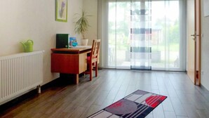 Una sala de estar moderna con piso de madera, una mesa de comedor, una silla, un radiador, una planta en maceta y un piso de vidrio corredera que da a un balcón.