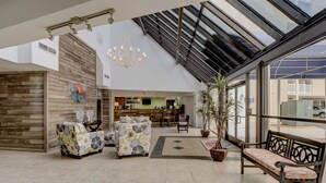 A spacious lobby with a high ceiling, a chandelier, a seating area with sofas and a bench, and a view through large windows to the outside. - 🌊Labor Day Available! Aug 30-Sept 3🔥Oceanfront🏝️2 Pools🐬Restaurants Onsite☀️ (North Topsail Beach)