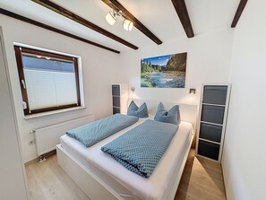 A bedroom with a bed, a window with blinds, a radiator, a painting, and a built-in wardrobe.