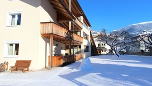 A multi-story building with wooden balconies, a snow-covered ground, and a mountain backdrop. - Cosy apartment for 8 guests with WIFI, TV and patio (Taxach)