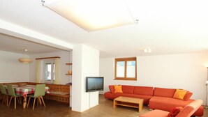 A spacious living area with a wooden dining table, a sofa, and a television. - Cosy apartment for 8 guests with WIFI, TV and patio (Taxach)