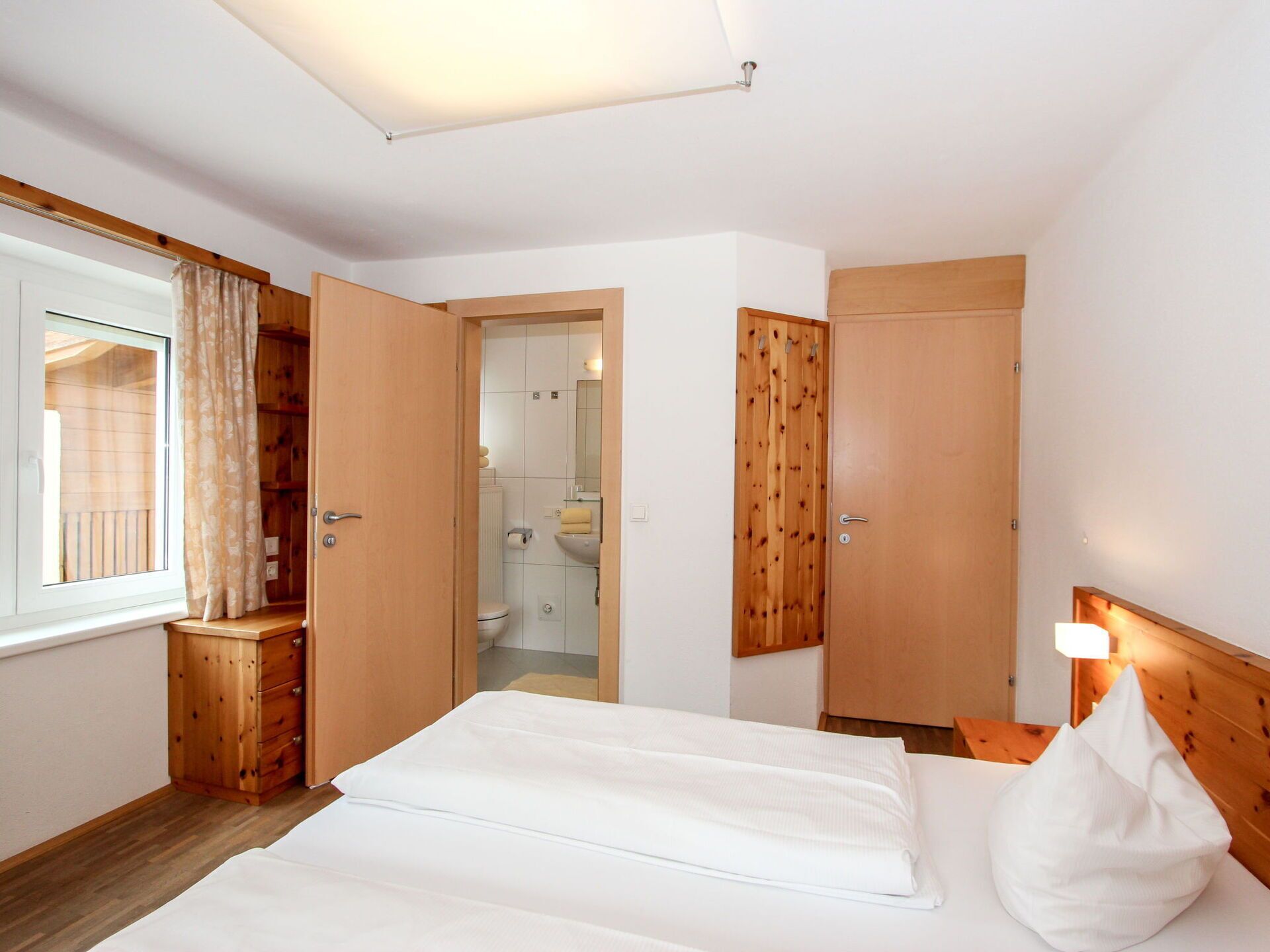 Un dormitorio con una cama, un armario de madera y un baño visible a través de una puerta abierta.